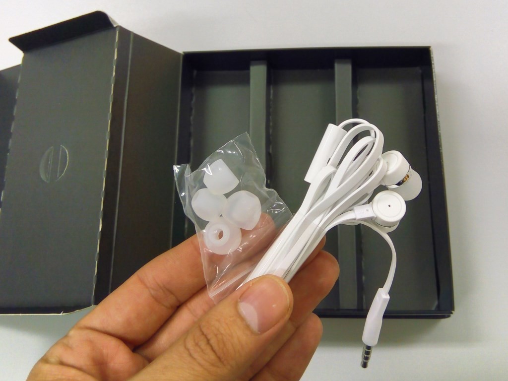 Fones de ouvido intra-auriculares, com microfone no cabo e um jogo de "borrachinhas" para adaptá-lo à sua orelha.